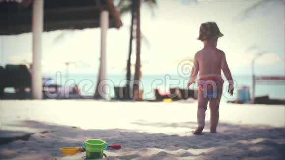 两岁的蹒跚学步的小男孩走在夏天的沙滩上在热带的沙滩上沿着沙子慢动作视频的预览图