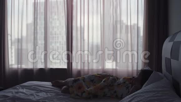 漂亮的年轻女人穿着裙子站在床上打开窗帘早上醒来慢动作视频的预览图