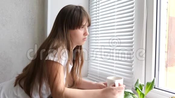 美丽悲伤的女孩望着窗外喝茶或咖啡视频的预览图