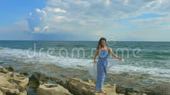 幸福美丽的女人站在岩石般的海滩上泡沫般的海浪拍打着海岸视频的预览图