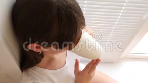 美丽的女孩坐在靠近窗户的窗台上喝着柠檬茶视频的预览图