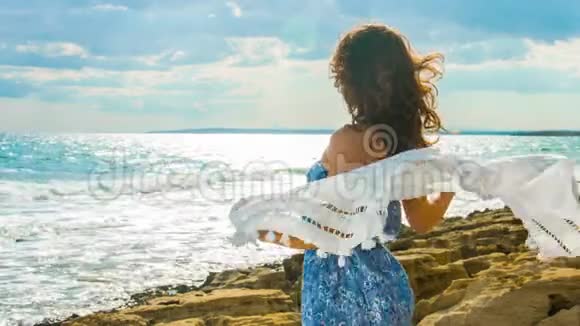 美丽的黑发女郎浪漫的心情站在海滩上享受着多风的天气视频的预览图