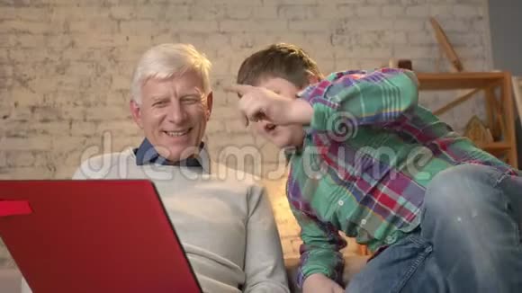 爷爷和孙子坐在沙发上在笔记本电脑上看有趣的电影笑着居家舒适视频的预览图
