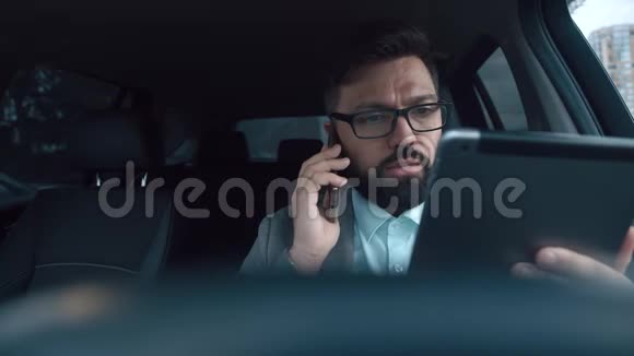 一个留着胡子的商人在打电话看着平板电脑视频的预览图