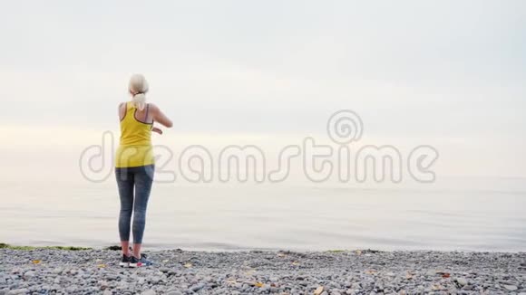 一个穿着黄色T恤的女人在湖或海的岸边取暖视频的预览图