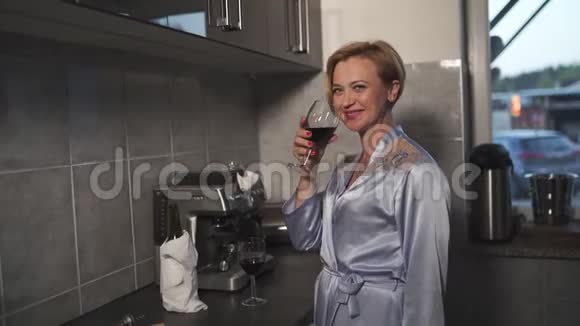 穿着蓝色早礼服的单身女人在厨房里喝着酒杯里的红酒笑着笑着视频的预览图