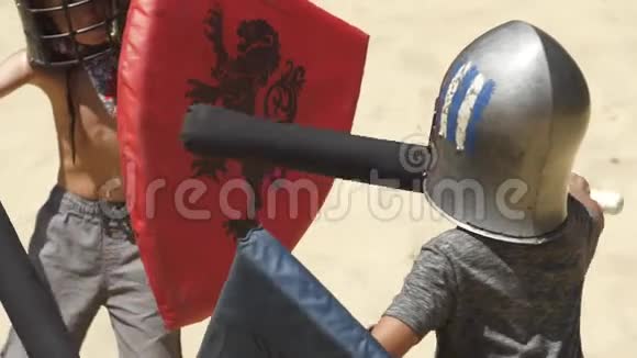 穿着塑料盔甲的男孩在竞技场上训练用棍子击剑孩子们游戏慢动作视频的预览图