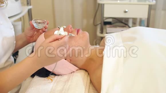 一个美容师用刷子在年轻女孩脸上敷面膜的特写视频的预览图