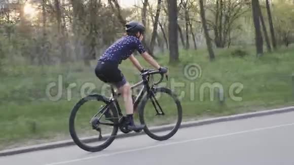 穿着蓝色球衣和黑色头盔的女孩在公园里骑自行车公路自行车训练自行车的概念慢动作视频的预览图