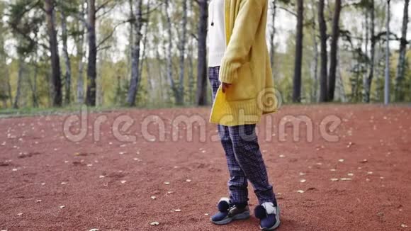一个穿着黄色毛衣的年轻女子在秋天公园散步腿和毛衣特写在秋天公园跳舞的女人视频的预览图