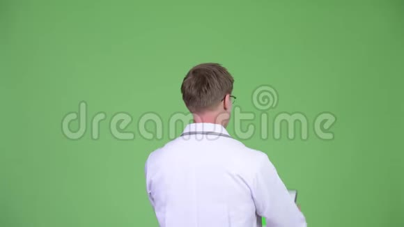 使用带有彩色按键绿色屏幕的数字平板的男性医生的后视图视频的预览图