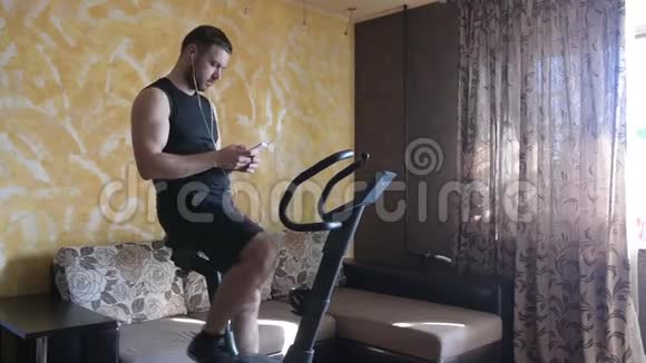 男人在家里训练运动自行车和使用智能手机视频的预览图
