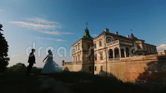 迷人的新婚夫妇的剪影轻轻地亲吻着古老城堡的背景视频的预览图