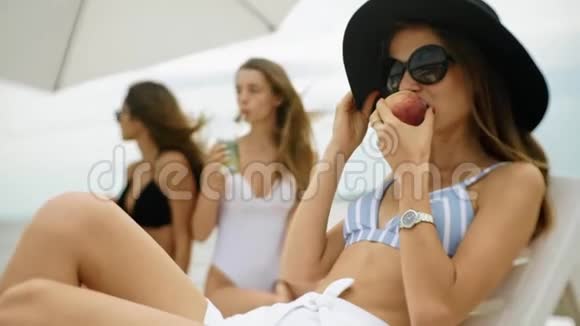 穿着泳装戴太阳镜的年轻漂亮女孩咬着桃子微笑着视频的预览图
