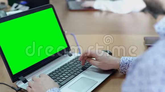 在办公室办公桌上用绿色屏幕的笔记本电脑工作的男性雇员视频的预览图