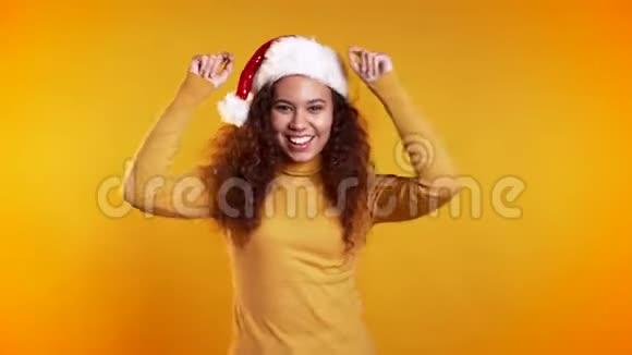 年轻可爱的女孩微笑着在黄色的工作室背景上跳舞戴圣诞帽的女人视频的预览图