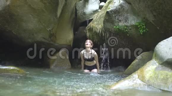 在绿色的热带森林中美丽的女孩用手在湖水上溅起瀑布巨石视频的预览图