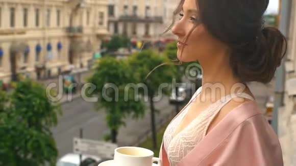 早晨的新娘一个穿着粉红色丝绸长袍的年轻女子站在阳台上为婚礼做准备视频的预览图