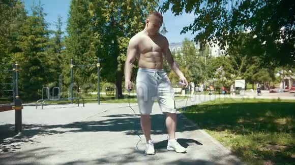 运动型肌肉男用绳子跳跃在阳光明媚的日子在户外锻炼慢动作视频的预览图