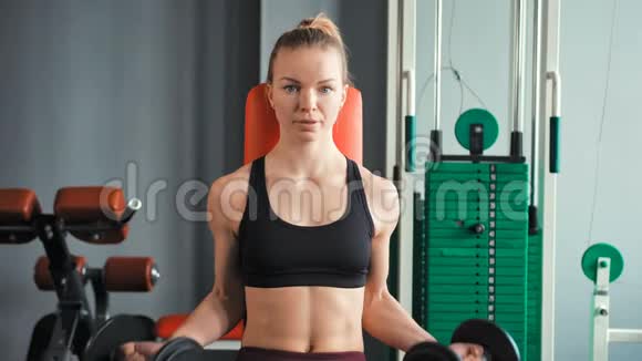 运动的年轻女子在健身房用哑铃锻炼视频的预览图