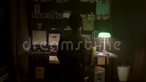 一个男人坐在办公桌前双手放在头后在黑暗的房间里放松库存休息的年轻人视频的预览图