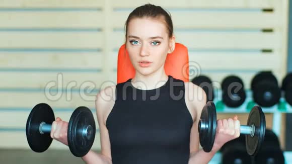 运动的年轻女子在健身房用哑铃锻炼视频的预览图