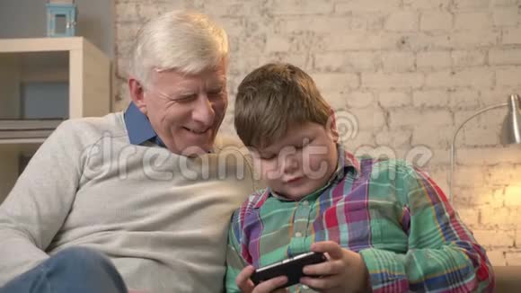 祖父和孙子坐在沙发上用智能手机说着一个胖孩子在玩智能手机视频的预览图