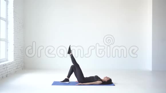 完整的视角健康的运动妇女躺在运动垫和抬起她的腿在白色工作室4k视频的预览图