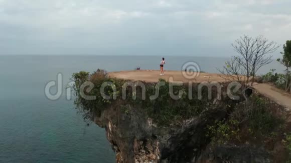 日出时在海边悬崖上伸展的女性鸟瞰图视频的预览图