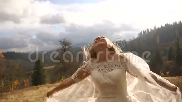 有趣的微笑新娘正高兴地摇头在阳光明媚的金山上玩她的面纱视频的预览图