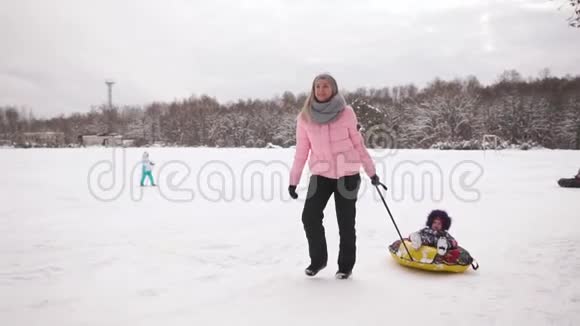 快乐的妈妈和女儿在冬天的雪中雪橇玩雪球母亲和孩子笑着快乐地滑行视频的预览图