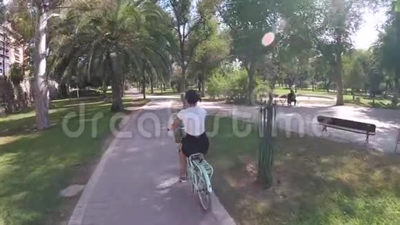 在公园棕榈树上骑自行车的女孩阳光慢动作视频的预览图