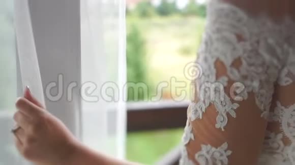 敏感美丽的新娘穿着完美的婚纱和面纱体贴地透过窗户看视频的预览图
