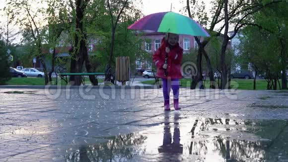 日落时分可爱的小女孩带着五颜六色的雨伞在公园的水坑里奔跑视频的预览图