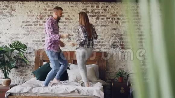 快乐的年轻恋人在床上跳舞在家里的卧室里玩得很开心漫不经心地笑着快乐的人现代的视频的预览图
