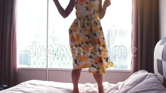 年轻快乐的女人穿着漂亮的裙子在酒店的床上跳舞慢动作3840x2160视频的预览图