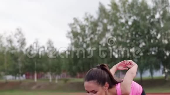 一个穿着粉红色T恤的女孩在慢跑前在体育场热身视频的预览图