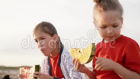 日落时两个女孩吃黄色和红色的西瓜一个漂亮的小女孩吃着一种罕见的黄色西瓜视频的预览图