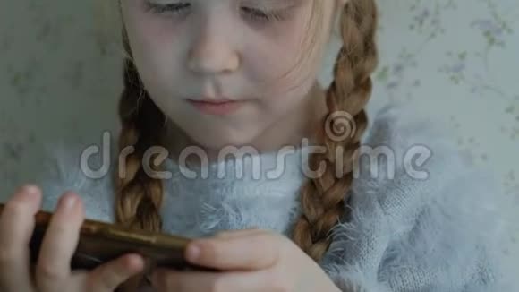 快乐的小女孩扎着辫子用电话玩微笑坐在房间的窗台上画像视频的预览图