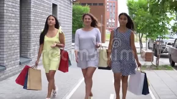 三个漂亮的女朋友购物后带着包裹沿着街走慢动作视频的预览图