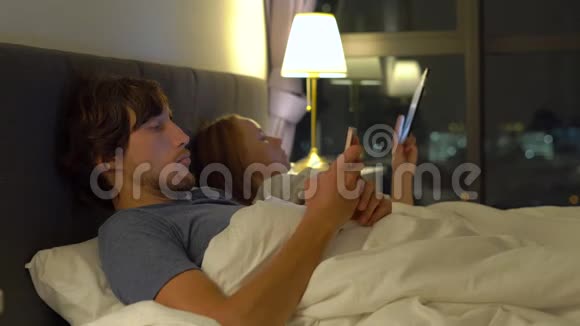 男人和女人躺在床上每个人都有智能手机和平板电脑女人关掉灯男人睡觉视频的预览图