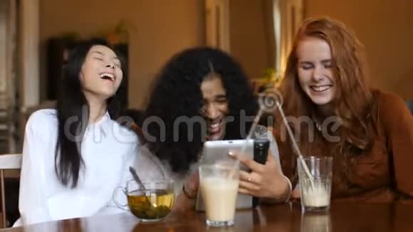 多民族女孩嘲笑电话平板电脑和咖啡馆视频的预览图