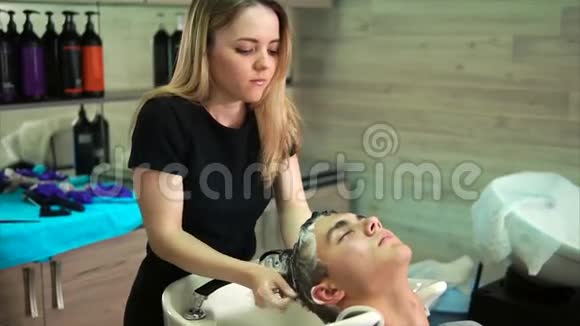 一位年轻的理发师用洗发水给一家美容院的访客负责人洗头发视频的预览图