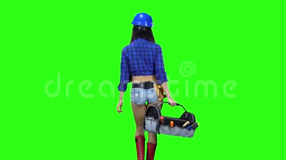戴着帽子和短裤的女孩的后景手里拿着一盒工具在绿色背景下行走视频的预览图