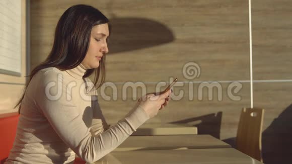年轻的黑发女人坐在有电话的咖啡馆里虚拟通信视频的预览图