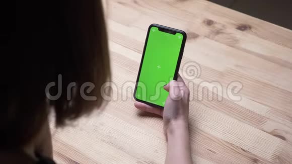 室内办公室办公桌上的女性手拿着一部带有绿色屏幕的手机的特写后景拍摄视频的预览图