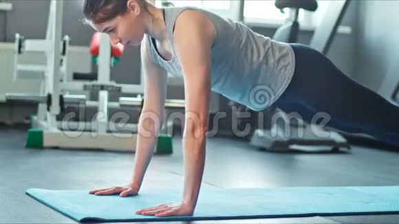 年轻女子在健身房的运动垫上做俯卧撑在健身房健身垫上运动的女性视频的预览图