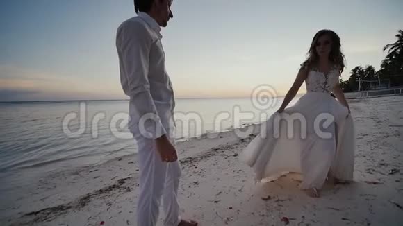 新娘和新郎在美丽的热带海滩上日落新娘在新郎面前跳舞紧紧抓住视频的预览图