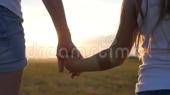 母亲和女儿在日落时在草地上散步和牵手妈妈的双手紧紧地抓住视频的预览图