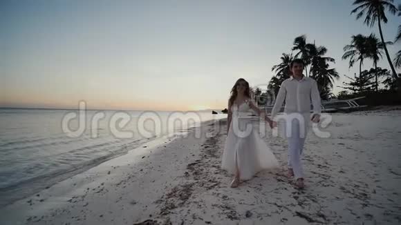 在海边日落时新婚快乐他们赤着脚走在沙滩上手牵着手看着每一个人视频的预览图
